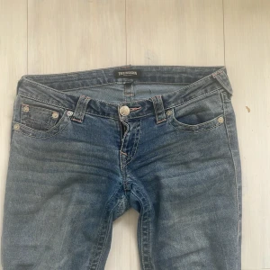 True Religion bootcut jeans blå - Säljer ett par blå jeans från True Religion med bootcut-modell och låg midja klippte av de på längden innerbenslängd 76 ja har lagat ett hål som syns på någon bild men det syns inte när man har på sig de