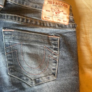 True Religion ljusblå bootcut jeans - Ljusblå jeans från True Religion med klassisk broderad bakficka och bootcut passform. Snygga kontrastsömmar och låg midja. Knappt använda och det finns inga fläckar eller revor.