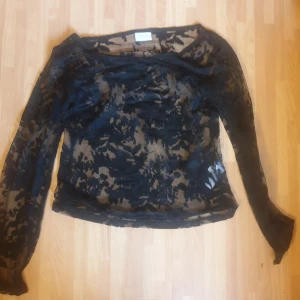 Svart meshblus från Vila med mönster - Säljer en transparent svart meshblus från Vila med lång ärm och snyggt blommigt mönster. Perfekt att styla lager på lager eller med ett linne under. Blusen har en figurnära passform och är riktigt trendig.