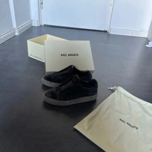 Svarta sneakers från Axel Arigato - Säljer ett par svarta sneakers från Axel Arigato. Skorna har en stilren design med rund tå och är tillverkade i mocka. De kommer med originalförpackning och dustbag. Perfekta för en trendig look.