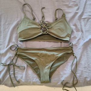 Olivgrön bikini med snörning från H&M - Snygg olivgrön bikini från H&M i storlek 36. Toppen har smala axelband och snörning framtill, medan bikinitrosan har knyt i sidorna för en justerbar passform. Perfekt för stranden eller poolen, enkel och stilren design.