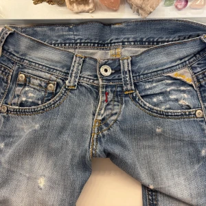Replay ljusblå lågmidjade jeans - Säljer ett par ljusblå lågmidjade jeans från Replay med slitna detaljer och raka ben. Innerbenslängd: 79cm, Midja rakt över: 38cm.