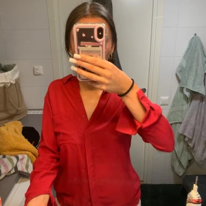 Röd skjorta med ficka och knappar - Snygg röd skjorta med klassisk krage och en bröstficka. Skjortan har långa ärmar och knappar framtill. Passformen är lite loose och tyget känns mjukt och följsamt, perfekt för en chill och stilren look.