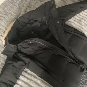 Svart dunjacka från Canada Goose - Säljer en svart dunjacka från Canada Goose med klassisk patch på ärmen och fuskpäls på huvan. Jackan har dragkedja, knappar och flera praktiska fickor. Perfekt för kalla vinterdagar och riktigt snygg streetstil.  Jackan är storlek M och är i riktigt bra skick // möts även upp inom Skåne pris kan sänkas vid snabb affär tveka ej att ställa frågor 