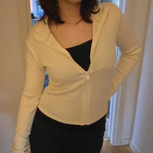 Beige stickad cardigan jacka med dragkedja - Säljer en beige stickad cardigan jacka med dragkedja framtill. Jackan är ribbad, har lång ärm och en snygg croppad passform. Perfekt för lager-på-lager och enkel att matcha med olika outfits.