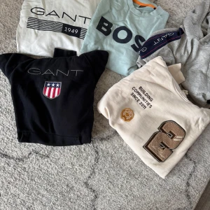 Märkeströjor paket - Svart hoodie från Gant med broderad logga och amerikanskt sköldmärke på bröstet. Klassisk huva och normal passform, perfekt för en chill och sportig look. Mjuk bomullskvalitet som känns skön mot huden.