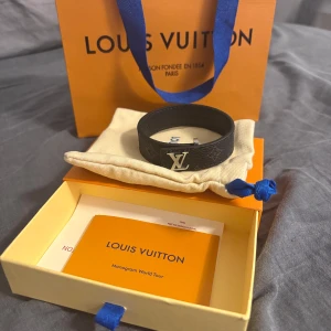Svart Louis Vuitton wrist band - Snyggt svart bälte från Louis Vuitton i äkta skinn med klassiskt LV-spänne i silver. Bältet har diskret monogrammönster och är tillverkat i Spanien. Perfekt accessoar för att lyfta din outfit med en lyxig touch.