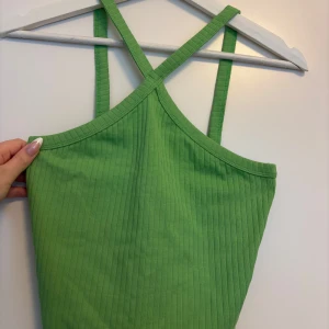 Grön ribbad linnetopp Gina Tricot - Snygg grön ribbad linnetopp från Gina Tricot med korsade axelband. Toppen är croppad och har en figurnära passform som sitter perfekt till jeans eller kjol. Tillverkad i mjuk bomullsmix som känns skön mot huden. Perfekt för dig som vill ha en fräsch och trendig look.