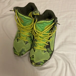 Gröna Under Armour basketskor strl 42,5 - Säljer ett par riktigt coola Under Armour basketskor i grönt och gult med camomönster. Skorna har högt skaft, gula snören och vit sula. Perfekta för dig som vill sticka ut med sportig stil. Materialet är syntet och mesh för bra andningsförmåga.