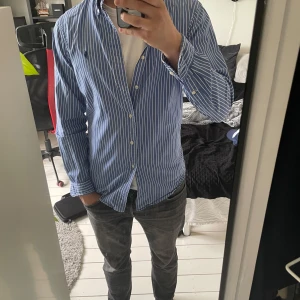 Blåvit randig skjorta Polo Ralph Lauren - Säljer en klassisk blå skjorta med vita ränder från Polo Ralph Lauren. Skjortan har lång ärm, knappar hela vägen och broderad logga på bröstet. Snygg krage och slim fit passform, perfekt till jeans eller chinos. Materialet är mjuk bomull. Har en liten färgbortfall över märket men som knappt syns.