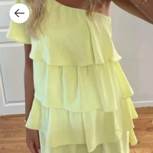 Ljusgul offshoulder volangklänning - Superfin ljusgul klänning med flera volanglager och offshoulder-design. Perfekt för varma dagar med sitt luftiga tyg och trendiga snitt. Klänningen har en kort längd och ger en riktigt somrig vibe.