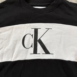 Svartvit Calvin Klein sweatshirt XS - Snygg svart och vit sweatshirt från Calvin Klein Jeans i storlek XS. Stor logga med 'cK' framtill och 'KLEIN' på ryggen, samt 'CALVIN JEANS' längs ärmarna. Tröjan har rund halsringning och är tillverkad i mjuk bomull.