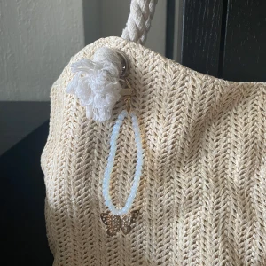 Väsksmycke/ Bag charm  - Säljer ett handgjord väsksmycke! Ljusblåa pärlor i kombination med en exklusiv guldfärgad fjärilsberlock. En subtil detalj som drar blickar åt sig och lyfter din outfit. Unik design, lätt att fästa och passar alla väskor. Perfekt även att ge som present till någon som älskar mode med personlighet. 