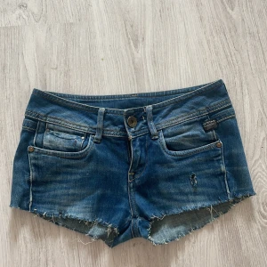 Blå jeansshorts från G-Star Raw - Snygga blå jeansshorts med låg midja, slitna detaljer och sömmar bak. Perfekta för sommaren! 