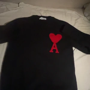Svart stickad tröja från Ami Paris - Svart stickad tröja från Ami Paris med ikoniskt rött hjärta och bokstaven A broderat på bröstet. Klassisk rund halsringning och långa ärmar. Perfekt för dig som vill ha en stilren men ändå unik look.