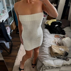 Vit axelbandslös kortklänning - Supersnygg vit axelbandslös kortklänning med tight passform och quiltad struktur. Klänningen har en enkel och stilren design som framhäver figuren, perfekt för dig som vill sticka ut. Materialet känns mjukt och följsamt mot kroppen.