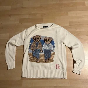 Vit stickad tröja Polo Bear Ralph Lauren - Vit stickad tröja från Polo Ralph Lauren med ikoniskt Polo Bear-motiv framtill. Tröjan har rund hals, ribbade muddar och RL 85-broderi nedtill. Perfekt för dig som gillar klassisk stil med en twist och vill sticka ut lite extra. Oanvänd, pris kan diskuteras, M men sitter som S