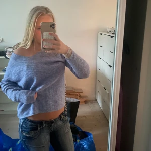 Ljuslila / pastell blå stickad offshoulder-tröja - Supermysig ljuslila stickad tröja med offshoulder-look och v-ringning. Tröjan har lång ärm och är lite croppad, perfekt att styla med jeans. Mjuk och skön, passar dig som gillar en chill vibe.