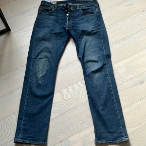 Levi's 501 blå jeans W33 L32 - Klassiska Levi's 501 jeans i mörkblå denim med raka ben och knappgylf. Snygg tvätt och ikoniska detaljer som läderpatch och röda Levi's-tag på bakfickan. Perfekta för en avslappnad och tidlös stil. 