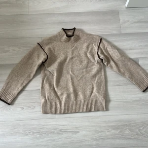 Beige stickad tröja från Primark XS - Beige stickad tröja från Primark i storlek XS. Tröjan har ribbad hög krage och muddar, samt bruna detaljer längs krage och axlar. Perfekt för lager-på-lager och chill höst- eller vinterstil.