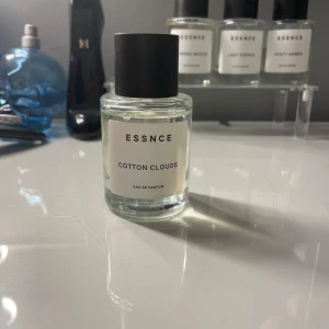 Essnce Cotton Clouds Eau de Parfum - Fräsch parfym från Essnce med namnet Cotton Clouds. Kommer i en stilren, rund glasflaska med svart lock och vit etikett. Doften är lätt och luftig, perfekt för dig som gillar rena och mjuka toner. Flaskan är transparent och minimalistisk i designen.