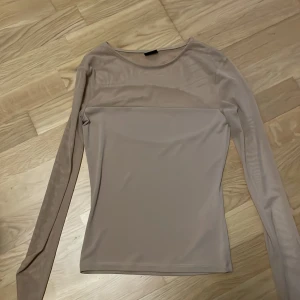 Beige meshtröja från Gina Tricot - Säljer en beige långärmad meshtröja från Gina Tricot. Tröjan har en transparent mesh upptill och är figurnära med rund halsringning. Perfekt att styla med jeans eller kjol för en trendig look. den är genomskinlig där uppe 