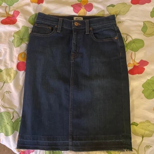 Mörkblå jeanskjol från J.Crew - Snygg mörkblå jeanskjol från J.Crew med klassisk femficksdesign och knappstängning fram. Rak modell som slutar strax ovanför knäna!