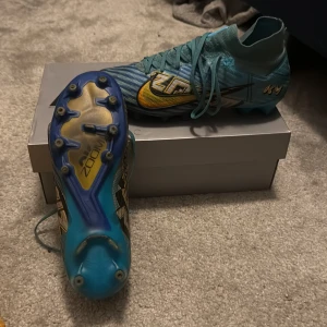 Nike Mercurial Zoom fotbollsskor blå/guld - Säljer ett par Nike Mercurial Zoom fotbollsskor i blått med guldiga detaljer och svart mönster. Skorna har snörning, platt sula med dobbar och en cool design. Kommer med originalkartong. Perfekta för dig som vill sticka ut på planen! Priset jag köpte 3,300 mitt pris 650kr