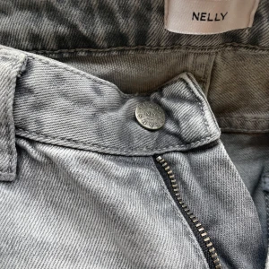 Gråa straight leg jeans från Nelly - Snygga ljusgrå jeans från Nelly i straight leg-modell med låg midja. Klassisk femficksdesign, dragkedja och knapp framtill. Tillverkade i mjuk bomull med lite stretch för extra komfort. Perfekta till en avslappnad och trendig look. 