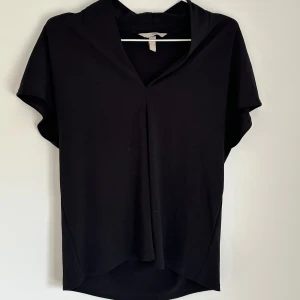 Svart blus med v-ringning från H&M - En svart blus från H&M med v-ringad hals och korta ärmar. Modellen är enkel och stilren med lätt avslappnad passform, perfekt att matcha med jeans eller kjol. Tunt och mjukt material som känns skönt mot huden.