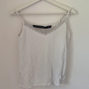 Vit linnetopp med spets från Black Label - Säljer en vit linnetopp från The Black Label Collection i storlek L. Toppen har tunna axelband och en snygg spetskant vid ringningen som ger en extra touch. Perfekt att styla med jeans eller kjol för en fräsch look.