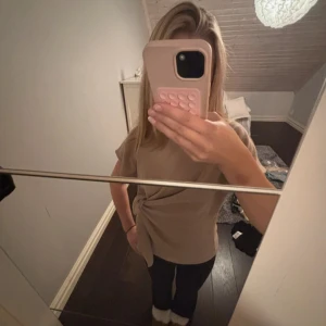 Beige topp med knyt i midjan - Säljer en beige topp med korta ärmar och snygg knytning i midjan. Modellen är rak och lite loose, perfekt för dig som gillar stilrena plagg med en twist. Materialet känns mjukt och skönt mot huden.