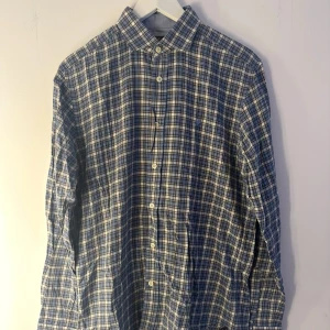 Morris skjorta  - En blå och vit rutig skjorta från Morris med långa ärmar. Skjortan har en knappslå och en liten logga på bröstet. Storlek M. Herr