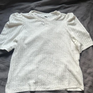 Vit blus med puffärm - Säljer en vit blus från Cubus med korta puffärmar och rund hals. Tyget har ett snyggt strukturerat mönster som ger toppen en unik känsla. Perfekt för dig som gillar stilrena och trendiga plagg med det lilla extra. Använd 1-2 gånger, normal i storleken och stretchigt material. 