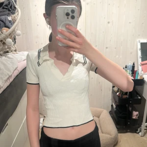 Vit ribbad topp från hm - Vit ribbad topp med v-ringning från H&M Divided. Toppen har svarta detaljer. Kortärmad och figurnära passform, perfekt för en sportig och trendig look.