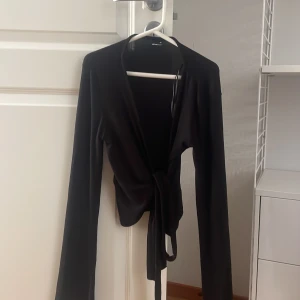 Svart omlottopp från Gina Tricot XS - Svart omlottopp från Gina Tricot i storlek XS. Den är i toppen skick. En knut tröja som är tunn och lång i armarna, den knyter man runt midjan.