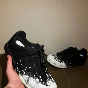 Maison margiela gats - Snygga svarta sneakers med unikt vitt färgstänk på ovandelen. Skorna har en klassisk snörning och en bekväm sula med bra grepp. Perfekta för en stilren och modern look. vill bli av med därav pris! Inget kvitto bara dustbags. Byten funkar.