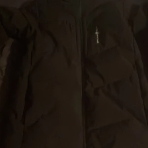 Svart dunjacka från Sail Racing - Säljer en svart dunjacka från Sail Racing. Jackan har en dragkedja framtill och är designad i Sverige. Den är fylld med 500 FP dun från Allied Feather + Down, vilket gör den perfekt för kalla dagar. Jackan har en stilren look med långärmade ärmar. Även sänka pris