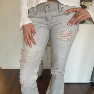 Hollister jeans - Snygga gråa bootcut jeans från Hollister med slitna detaljer och en låg midja. Tjejen som har på sig jeansen är 173cm och brukar ha storlek S, skriv vid funderingar🌸🌸