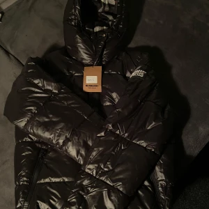 Svart pufferjacka från Burberry - Säljer en snygg svart pufferjacka från Burberry med klassiskt rutigt foder. Jackan har en hög krage med både dragkedja och knappar framtill. Den har även funktionen avtagbara ärmar så man får den till en väst :) Helt oanvänd och köpt här på Plick, tyvärr var den alldeles för stor :(. Hör av dig i DM vid intresse eller frågor :) 