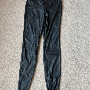 Svarta skinnbyxor från Esmara - Snygga svarta leggings från Esmara med en glansig finish. Perfekta för en stilren look och kan enkelt matchas med olika toppar. De har en elastisk midja för extra komfort. Storlek L 