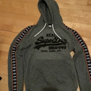 Grå Superdry hoodie - Riktigt snygg grå hoodie från Superdry. I princip nyskick. Öppen för prisförslag. Storlek M. Var inte rädd att fråga mig om du undrar något 😁