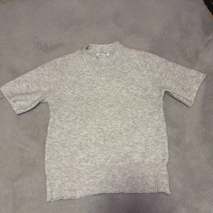 Grå stickad tröja från J'aime - Säljer en stilren grå stickad tröja från J'aime. Tröjan har korta ärmar och en rund halsringning, perfekt för en avslappnad look. Den mjuka stickningen gör den bekväm att bära hela dagen.