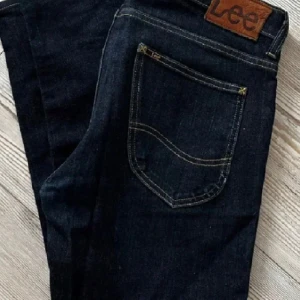 Mörkblå jeans från Lee - Snygga mörkblå jeans från Lee med klassisk femficksdesign och gul kontrastsöm. Perfekta för en stilren look. Märkeslapp i läder baktill. Prisnkan diskuteras vid snabb affär!