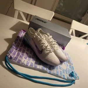 Nike air zoom mercurial vapor 16 elite  - Snygga vita Nike fotbollsskor med lila swoosh och blå detaljer på hälen. Skorna har snörning och en modern design som passar perfekt för fotbollsplanen. Levereras med en matchande påse. Har blivit använda 1 gång 👀🔥