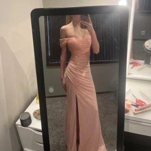 balklänning - Superfin elegant rosa långklänning med paljetter och offshoulder-design. Klänningen har en slits och inbyggd bh. Är köpt från Flormiss och säljer den för att överdelen var lite stor på mig. Den är i storlek xs men skulle säga att den är mer som en s. Pris går även att diskuteras. Skriv gärna om ni har några frågor om klänningen<3