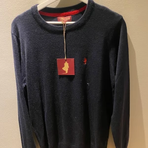 Mörkblå tröja från MCS - Säljer en stilren mörkblå tröja från MCS med en liten röd broderad logga på bröstet. Tröjan har långa ärmar och en rund halsringning med ribbade kanter. Perfekt för en avslappnad och snygg look. Aldrig använd 