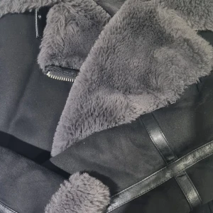 Svart jacka med fuskpäls från Zara - Snygg svart jacka från Zara med mjuk fuskpäls på insidan och kragen. Jackan har en dragkedja och stilrena detaljer i skinnimitation. Perfekt för kyligare dagar.