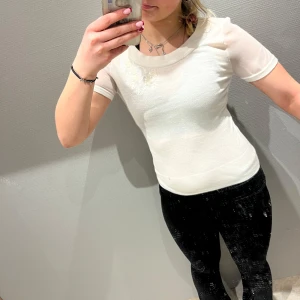 Vit kortärmad topp med broderi - Säljer en stilren vit topp med korta ärmar och vackert broderi på bröstet. Perfekt för en elegant och enkel look. Passar bra till både jeans och kjol.