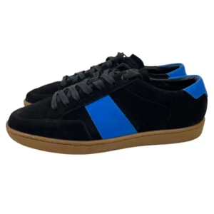 Saint Laurent skor Intressekoll - Snygga svarta sneakers från Saint Laurent med blå detaljer och brun sula. Skorna har en klassisk design med snörning och är tillverkade i mocka. Perfekta för en stilren look. I nyskick. Storlek 41 men sitter något mer som 42!👍🏼Obs endast Intressekoll👍🏼i